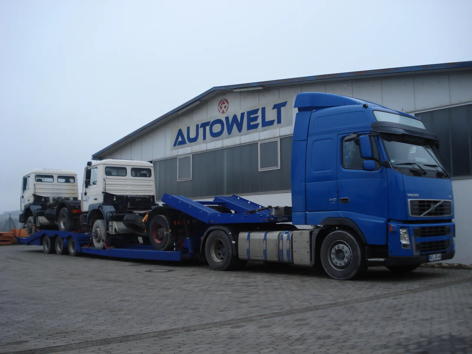 Autowelt-Tieflader mit zwei geladenen Nutzfahrzeugen vor der Werkstatt in Niederlauer
