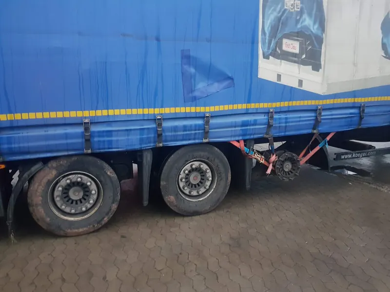 Kögel curtainsider semi-trailer with the wheel removed, the exposed wheel hub secured with straps